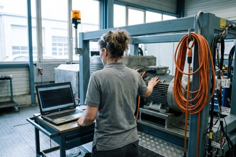 Ingenieurin am Prüfstand mit einer elektrischen Antriebseinheit und aufgeklapptem Laptop.