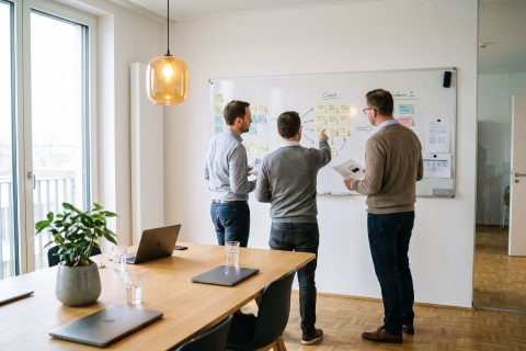 Drei Kolleginnen und Kollegen vor einer Kartenwand im Projektraum eines Dienstleisters.