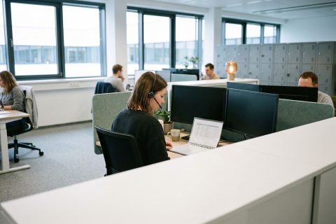 Mitarbeiterin mit Headset an einem aufgeräumten Arbeitsplatz einer offenen Servicefläche.
