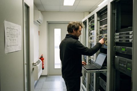 Techniker mit Laptop zwischen zwei Serverschränken im hauseigenen Technikraum.