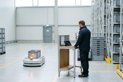 Koordinator beobachtet ein fahrerloses Transportfahrzeug im Gang eines automatisierten Lagers.