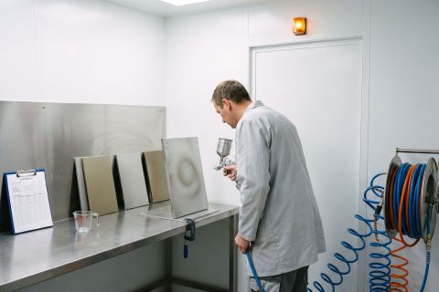 Techniker prüft in einer Musterkabine das Spritzbild einer Applikationsdüse an einem Testblech.