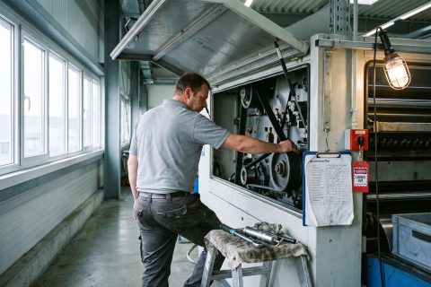 Instandhalter prüft einen Antriebsriemen an einer abgeschalteten Produktionsmaschine.