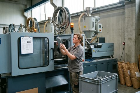 Bedienerin entnimmt ein frisch gespritztes Bauteil an einer Spritzgießmaschine.